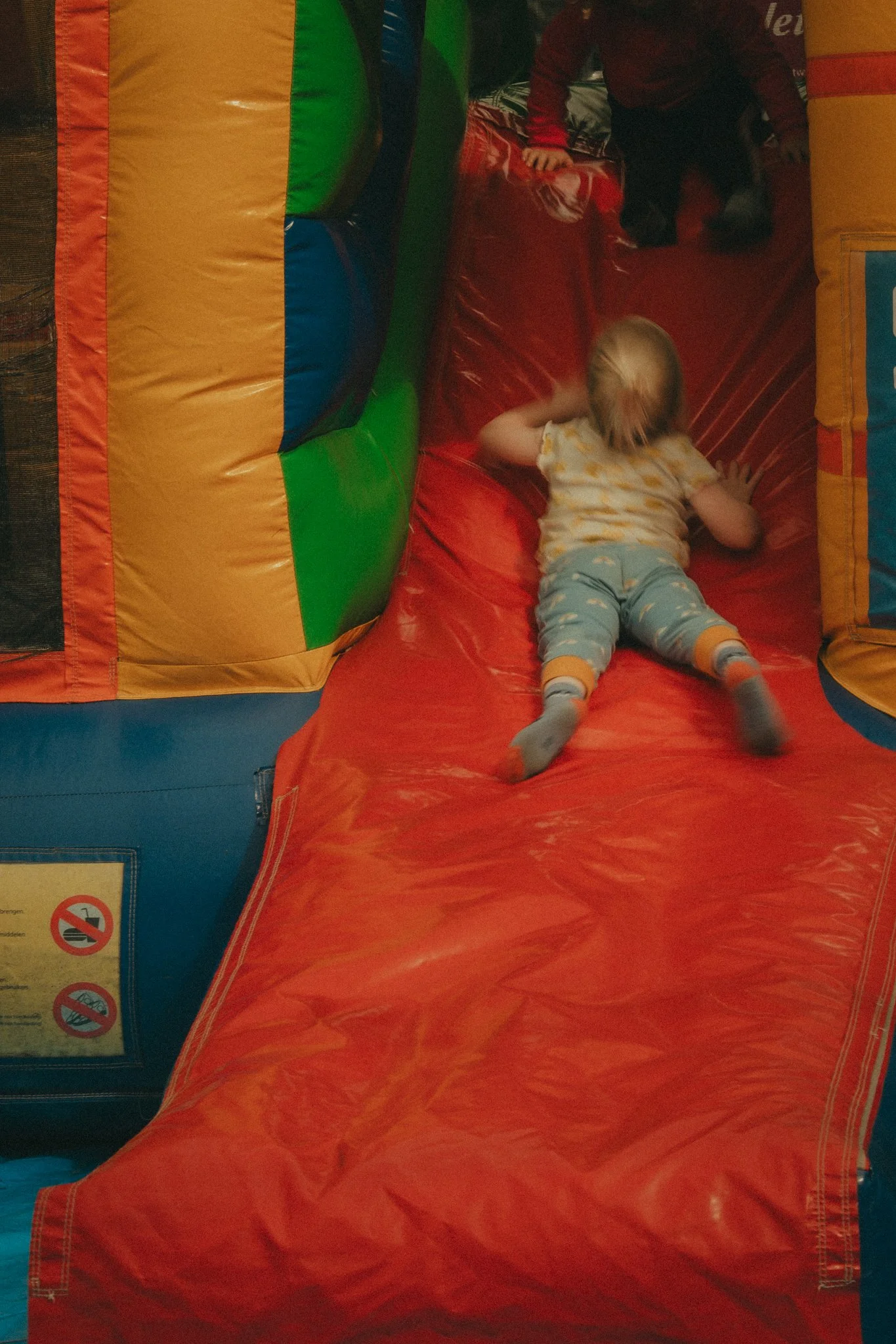 Children playing inside a colorful inflatable bounce house, with a girl lying down on the red inflatable surface and other children climbing or playing in the background.