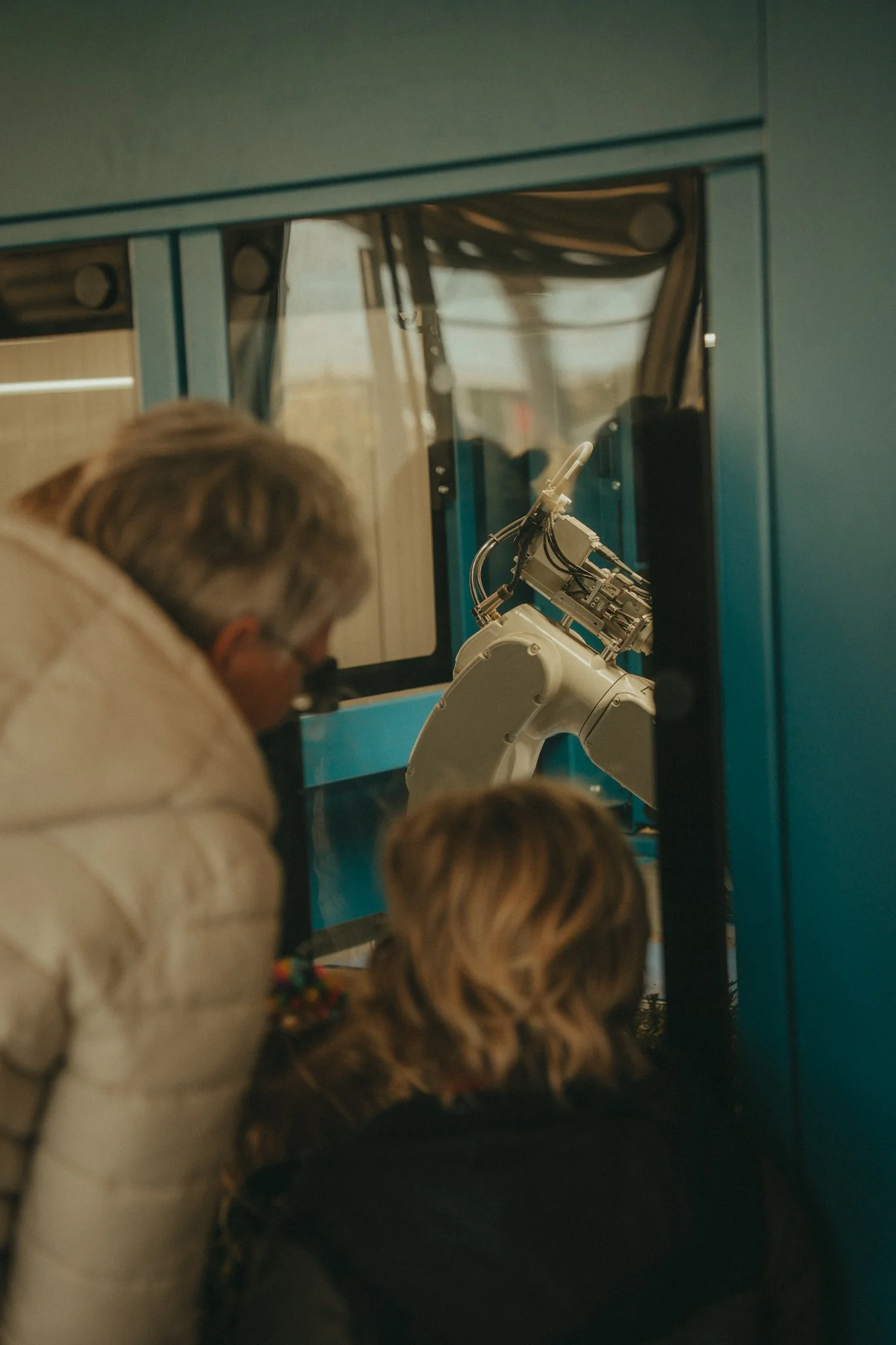 People observing a robotic arm through a glass window.