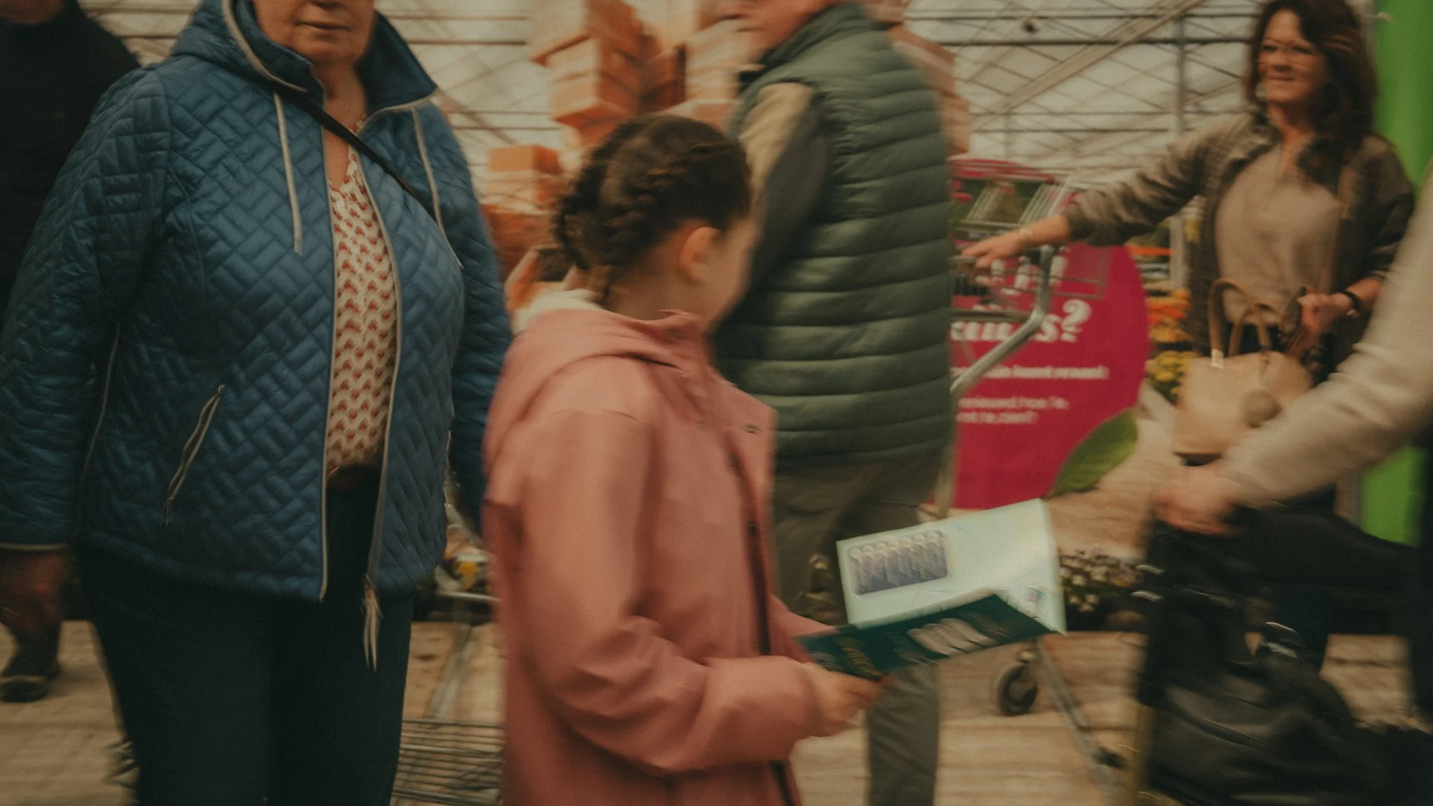 People shopping at a store, with a woman in a blue jacket and a girl in a pink hoodie looking at items on a table.