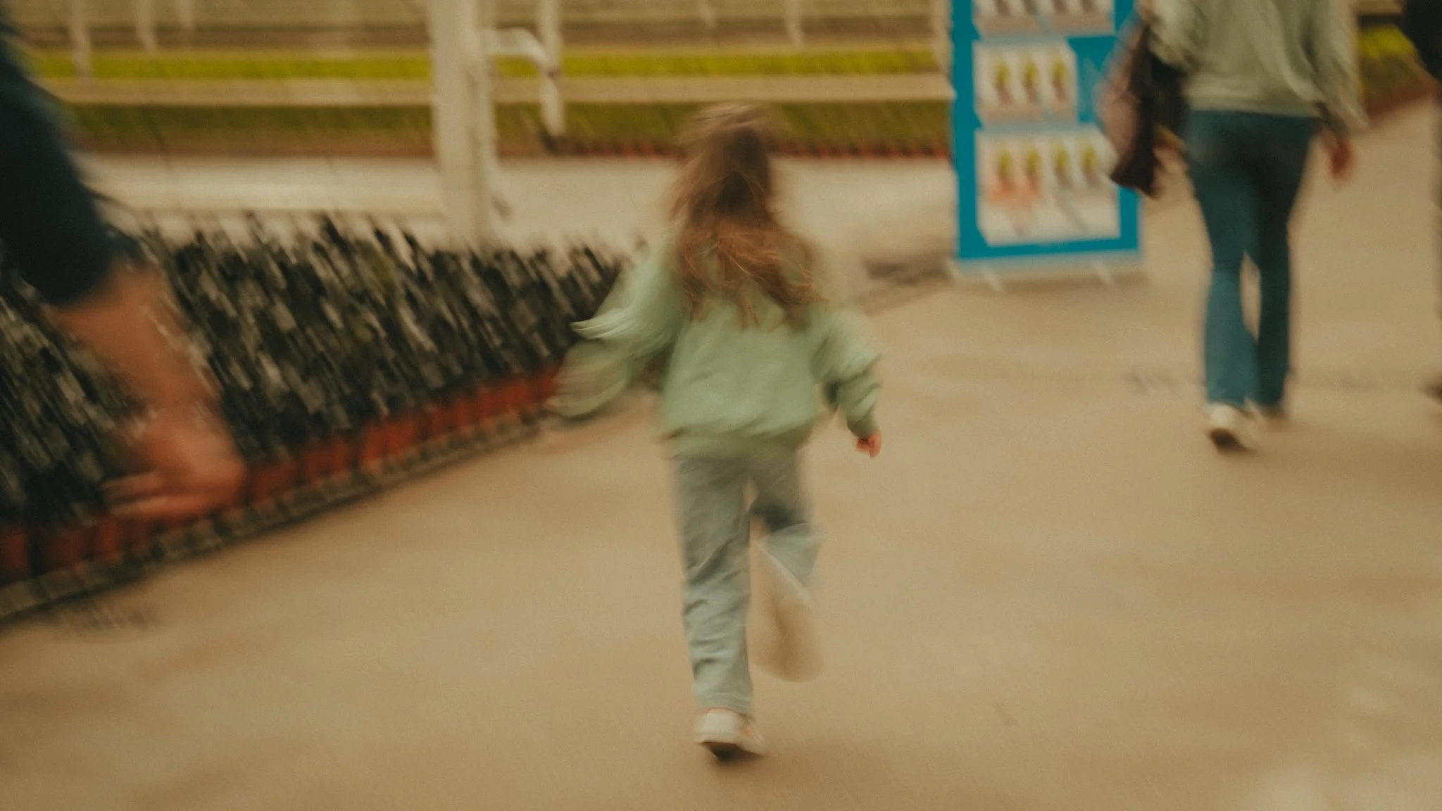 Child running in a store aisle with shelves and a blue display in the background.