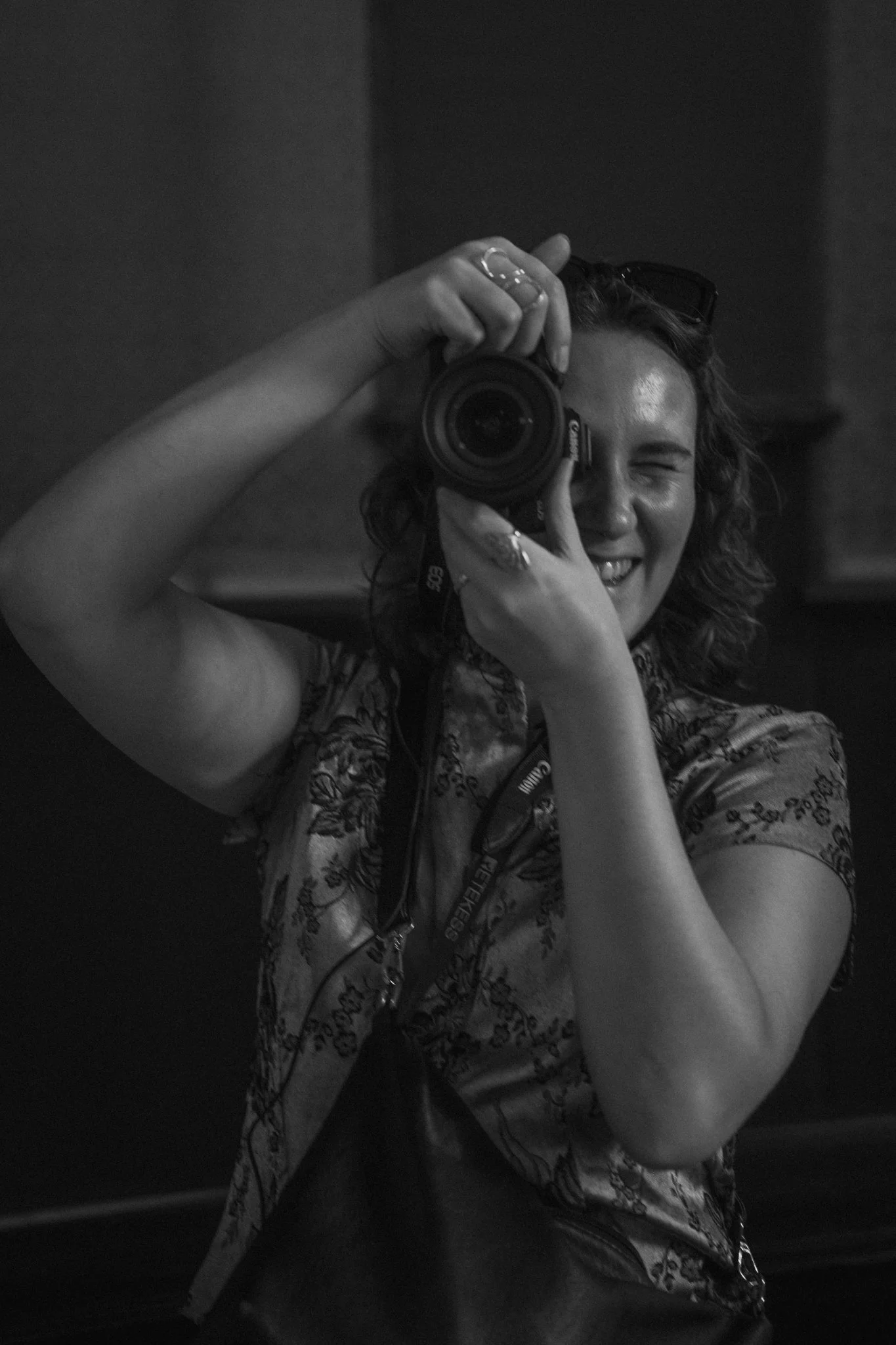 A woman taking a selfie with a camera, smiling with her eyes closed, in black and white.