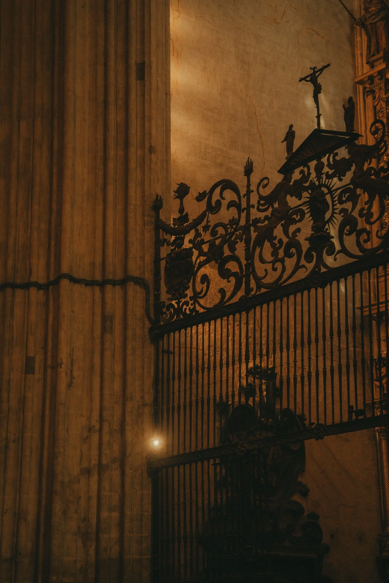 A penitential church with a highly detailed wrought iron railing, religious statues, and a crucifix on a wall illuminated with warm lighting.