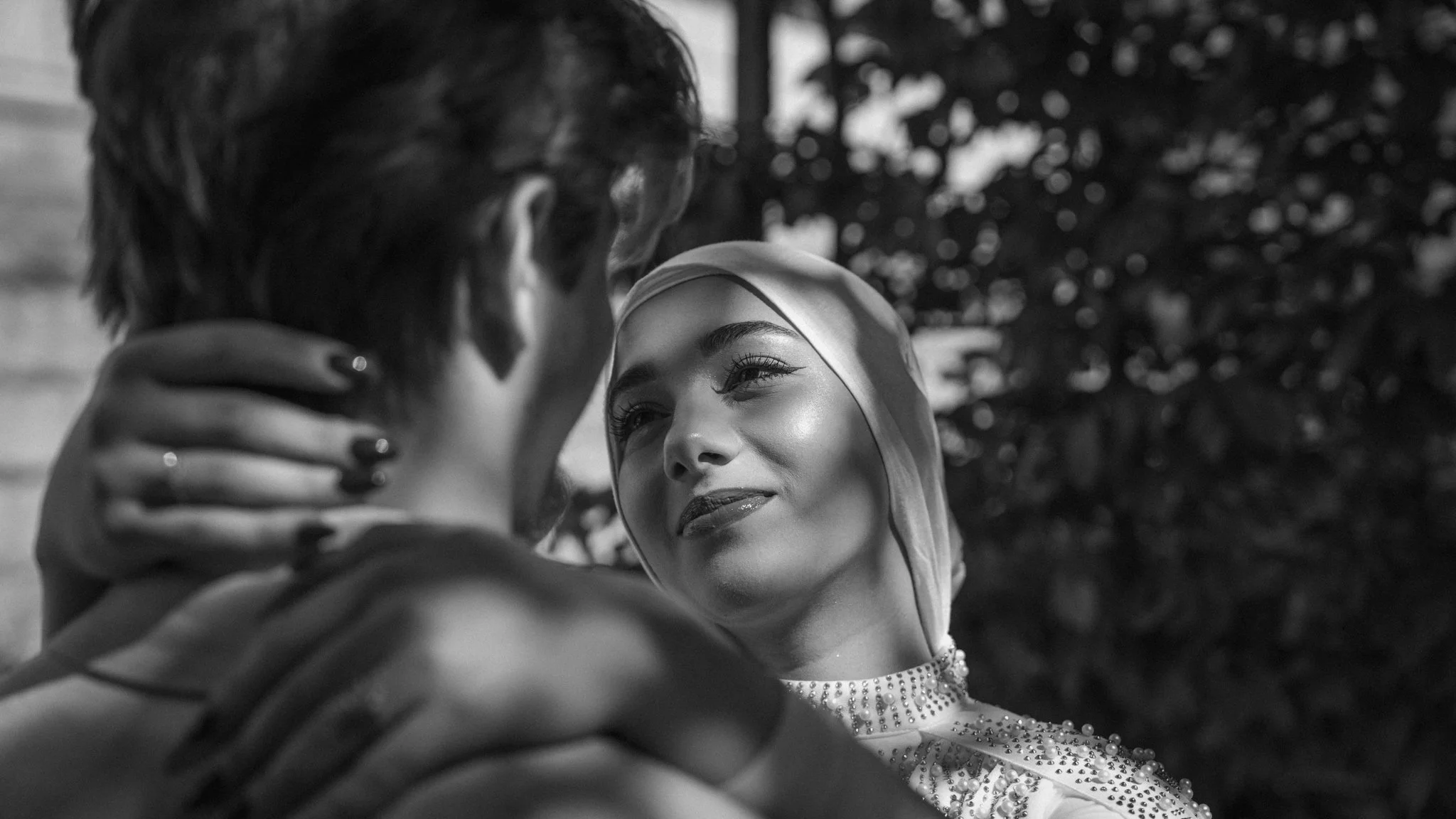 Black and white photo of a couple gazing into each other's eyes, with the woman wearing a headscarf and jewelry, and the man holding her face gently.