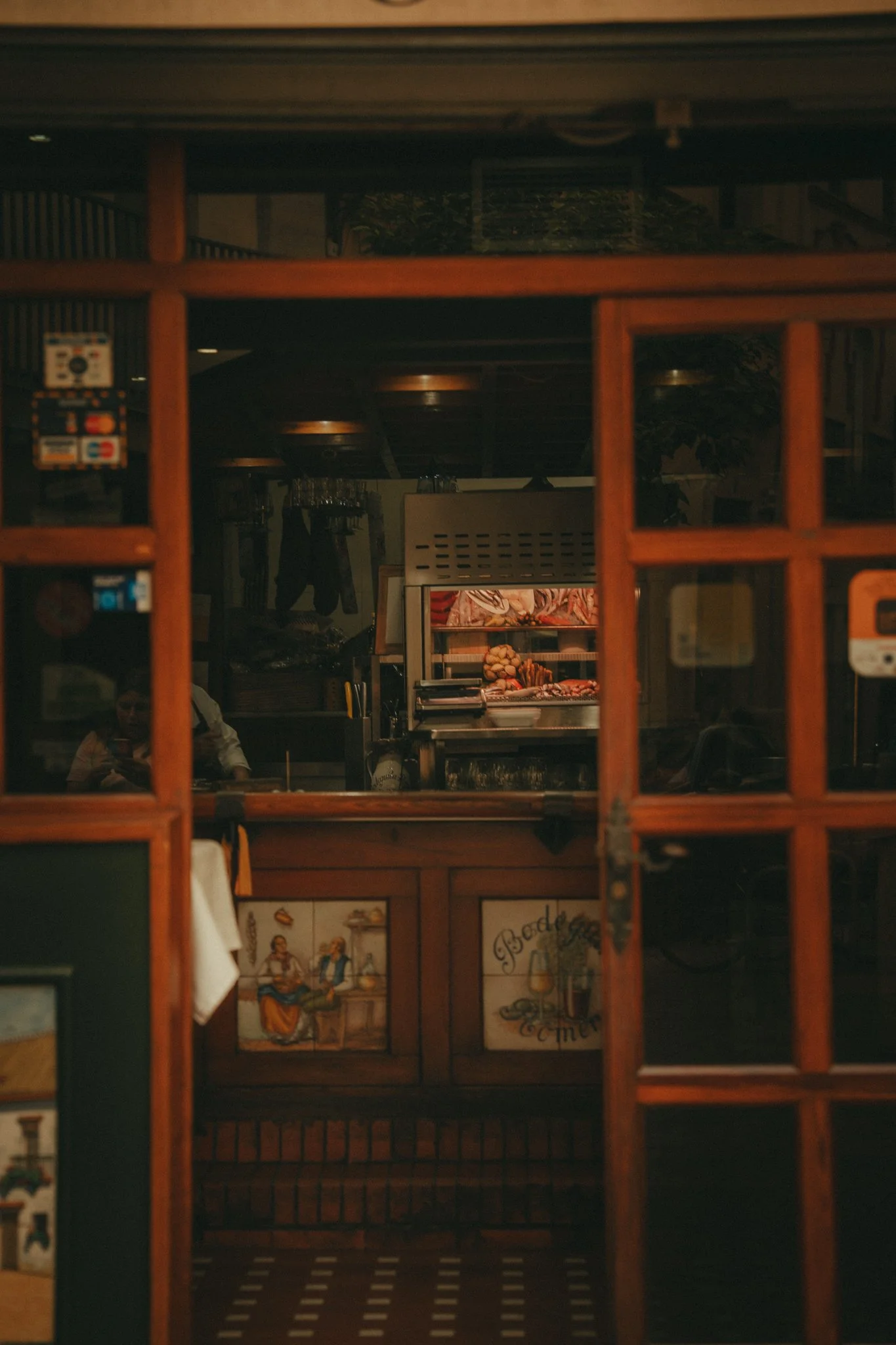 View through a wooden-framed window showing the interior of a restaurant or cafe, with a counter displaying baked goods and framed artwork on the wall.