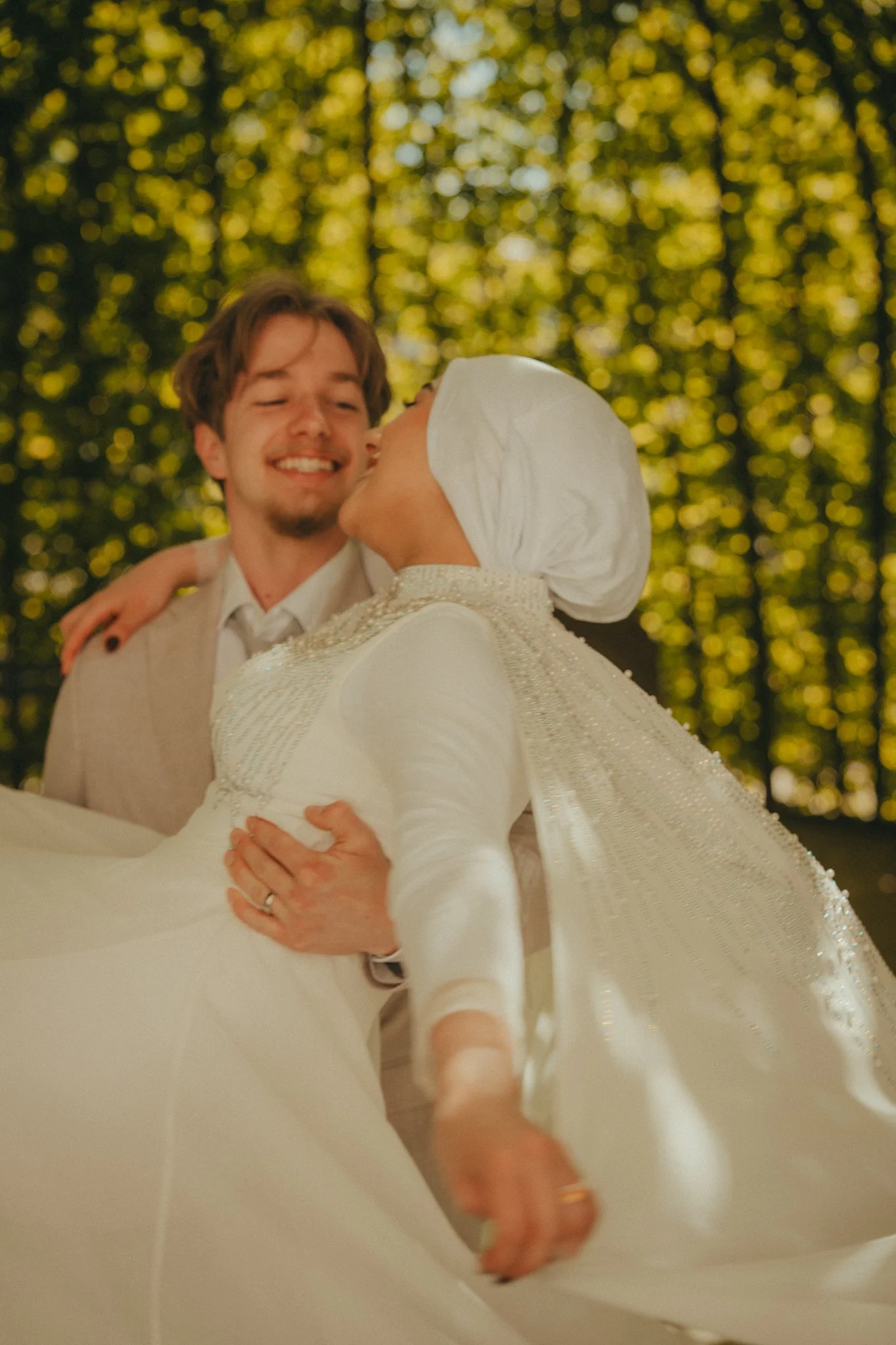A couple, dressed in wedding attire, dancing outdoors near trees with yellow leaves. They are smiling and holding each other closely.