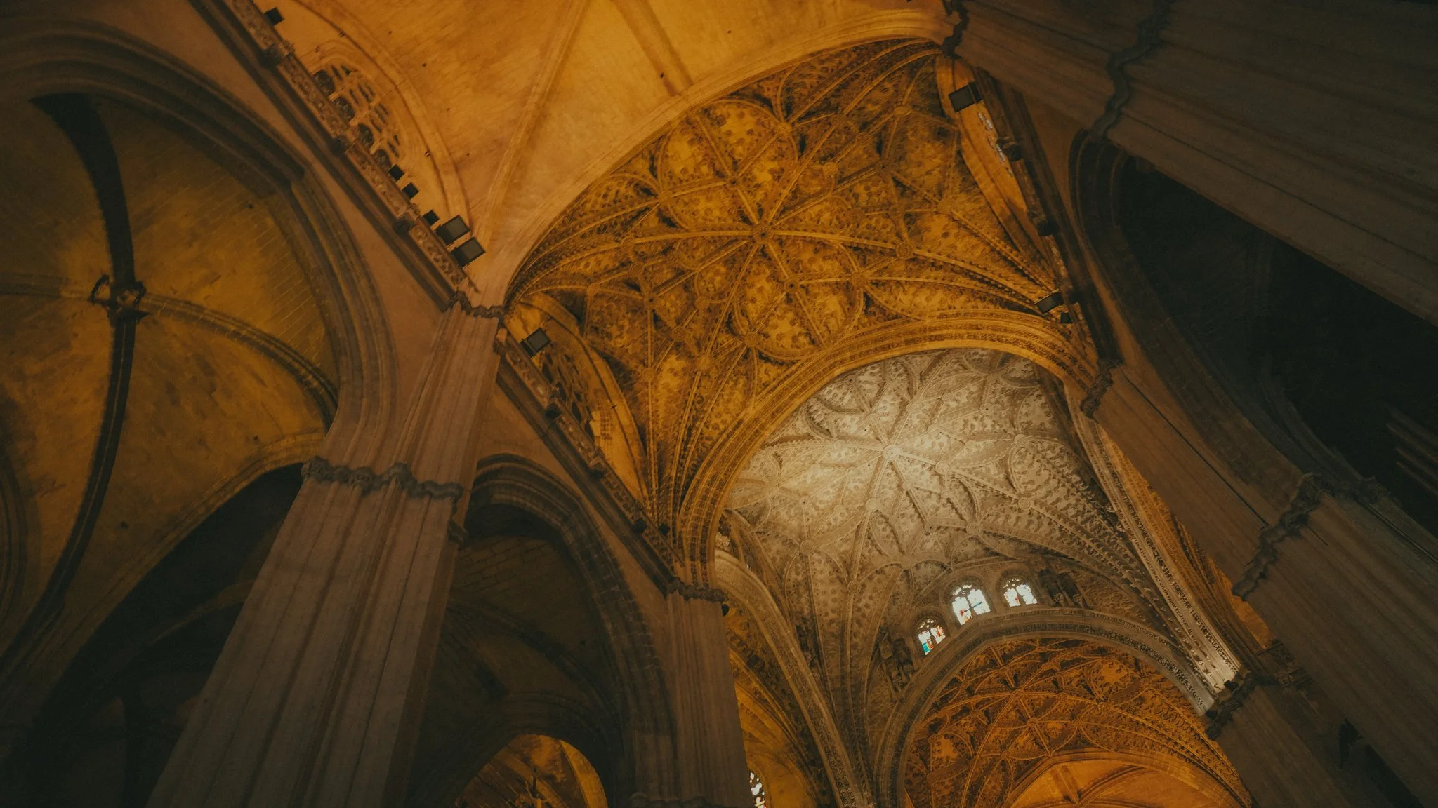 Interior view of a Gothic cathedral with high vaulted ceilings, ornate architectural details, and stained glass windows.