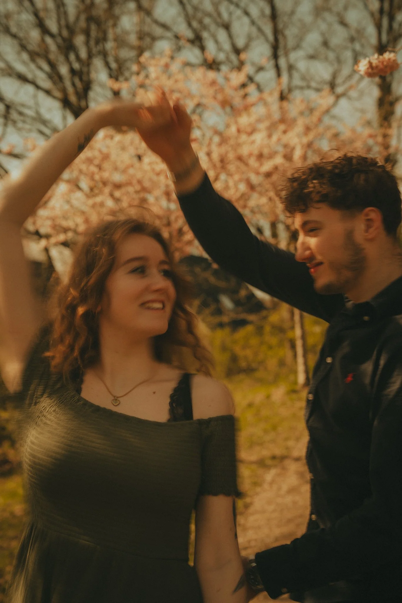 A young couple dancing outdoors with autumn trees and falling leaves in the background.