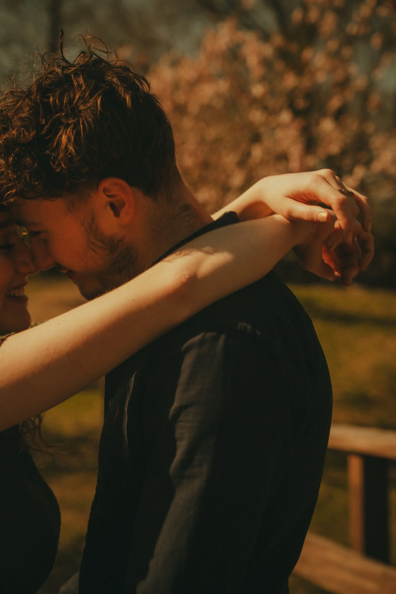 A couple sharing an intimate moment, with the woman hugging the man's shoulders from behind during nighttime.