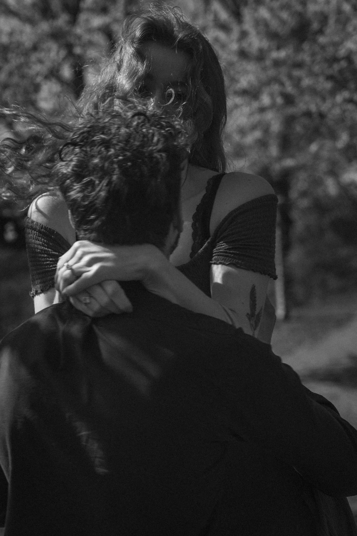 A black and white photo of two people embracing, with one person's face partially hidden and the other's face mostly obscured by hair. The scene appears to have been taken outdoors at night.