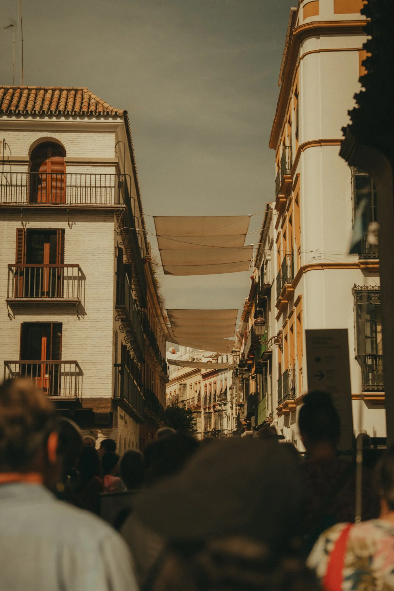 People gathered on a city street with buildings on either side, and fabric canopies hanging overhead, possibly during a festival or street event.