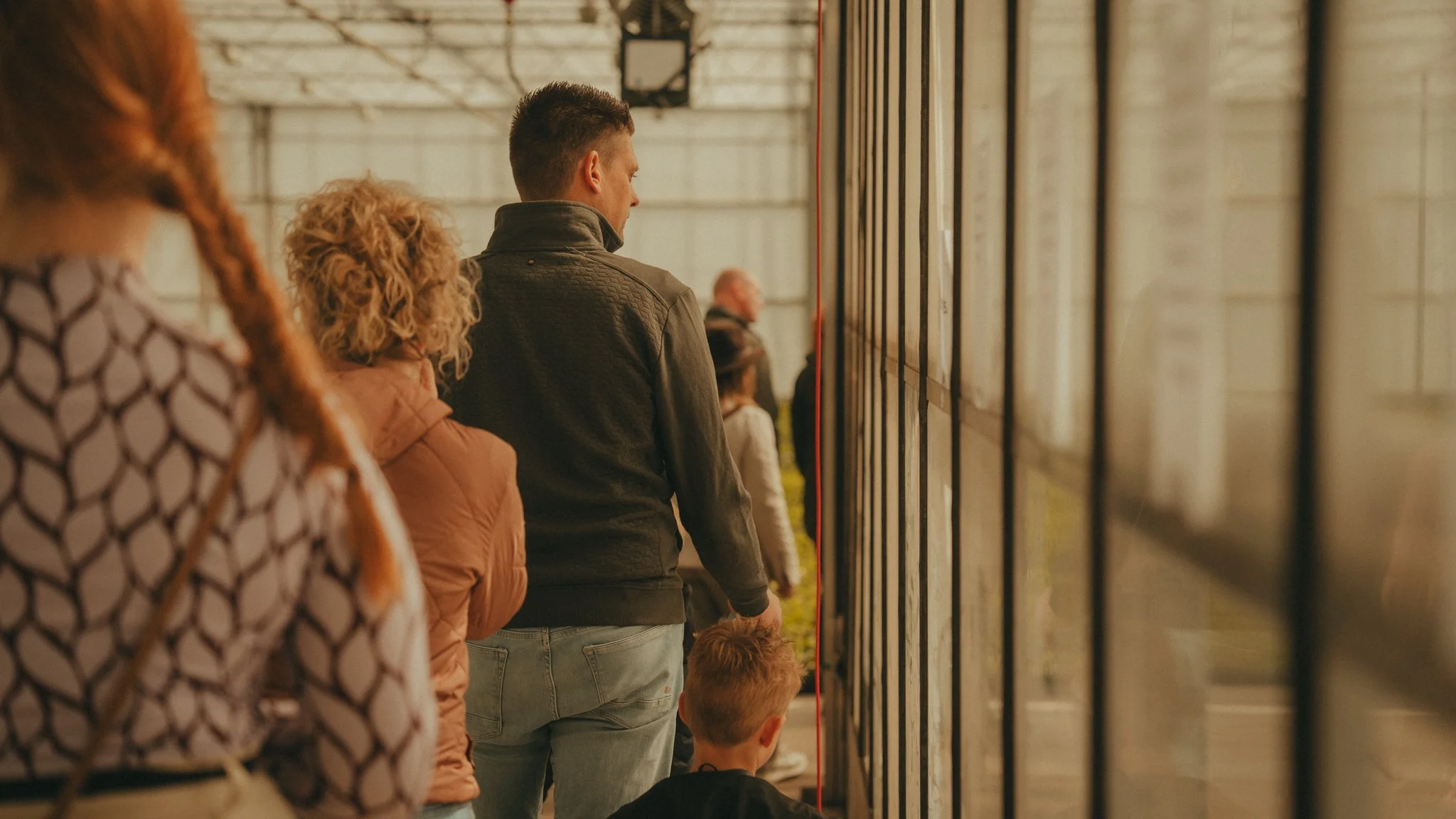 People line up to view artwork or photographs on a wall inside a gallery or exhibition space.
