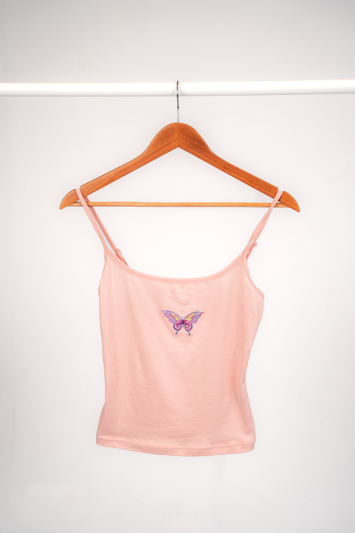 Pink sleeveless top with a butterfly embroidery hanging on a wooden hanger.