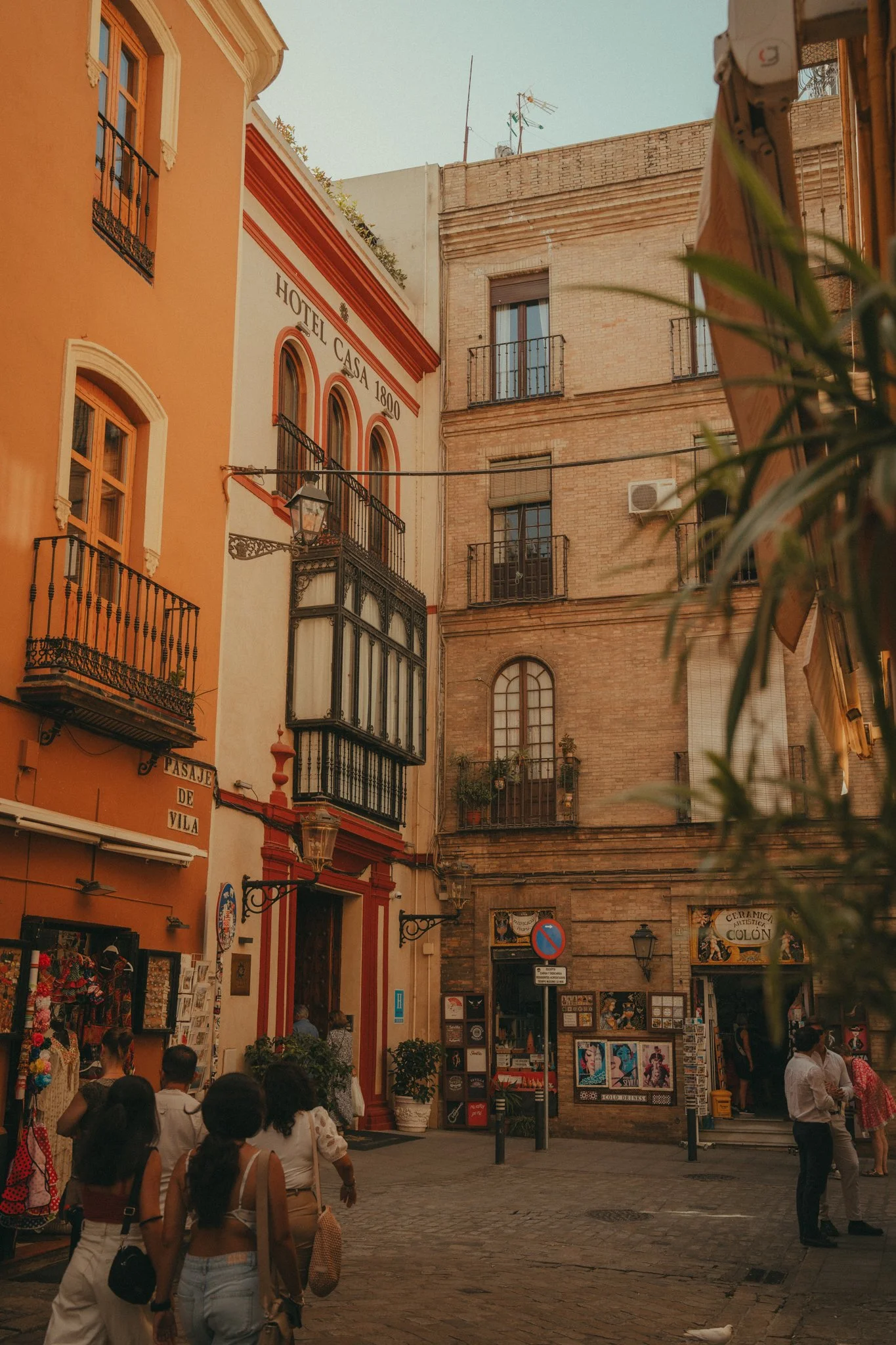 A busy street scene in a historic city, with colorful buildings, people walking, and shops selling souvenirs and artwork.