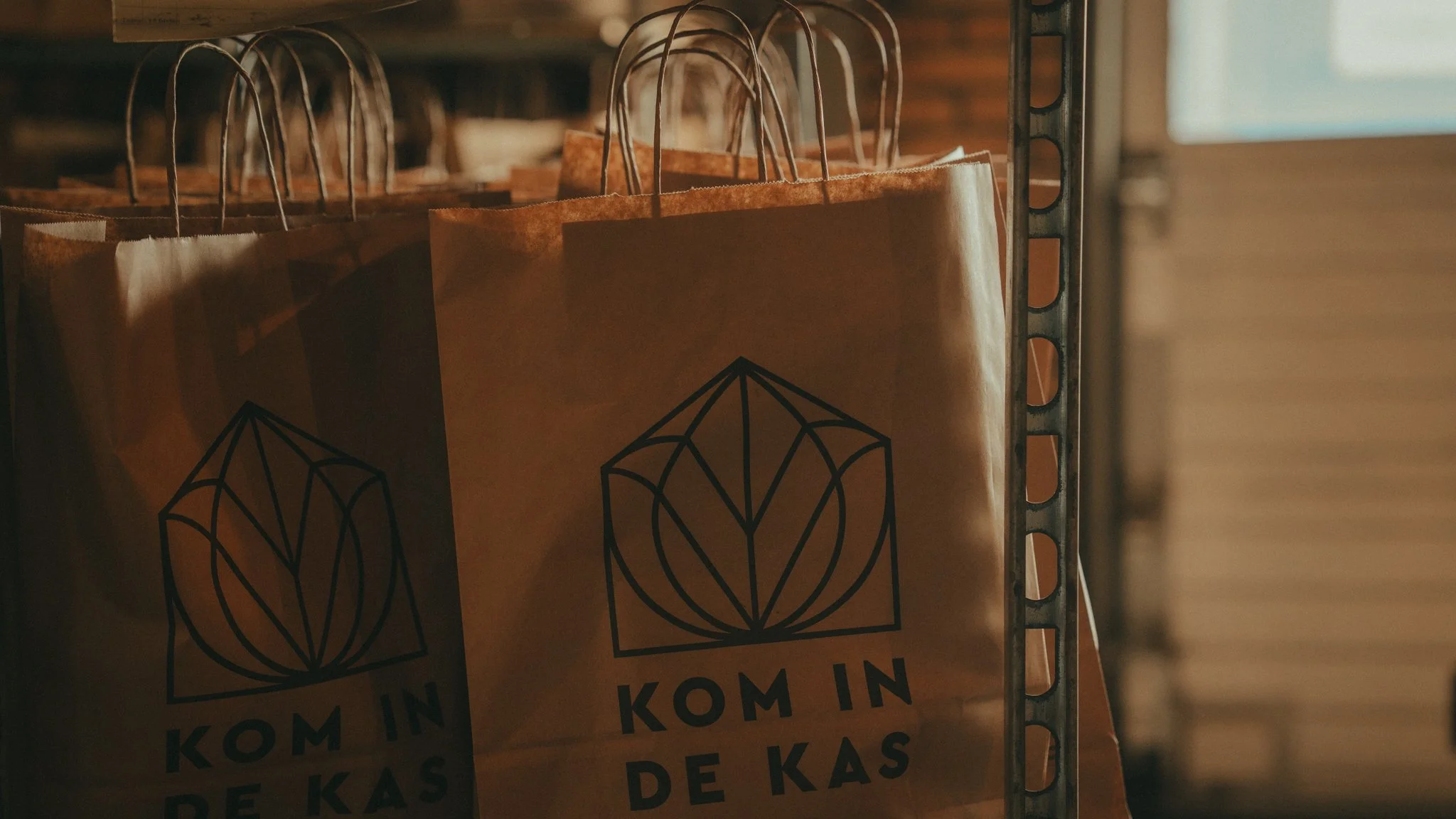 Brown paper bags with a black geometric logo hanging on a metal rack.
