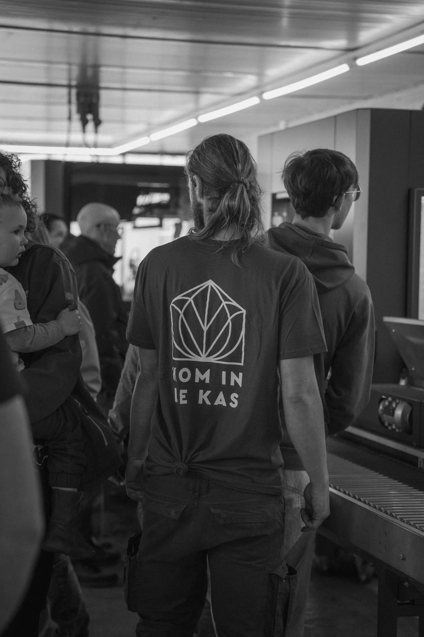 People gathered at an airport or train station, standing near a baggage conveyor belt, possibly waiting for luggage or transportation.