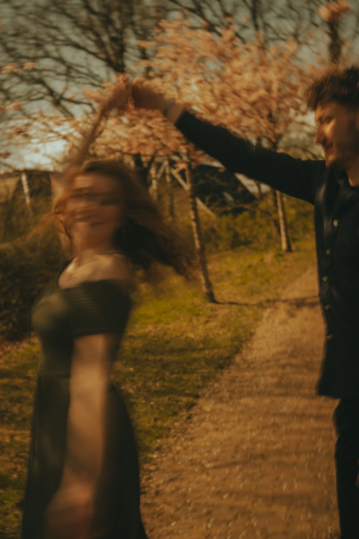 Two people in a park at night, seemingly playing or dancing under trees with fallen leaves