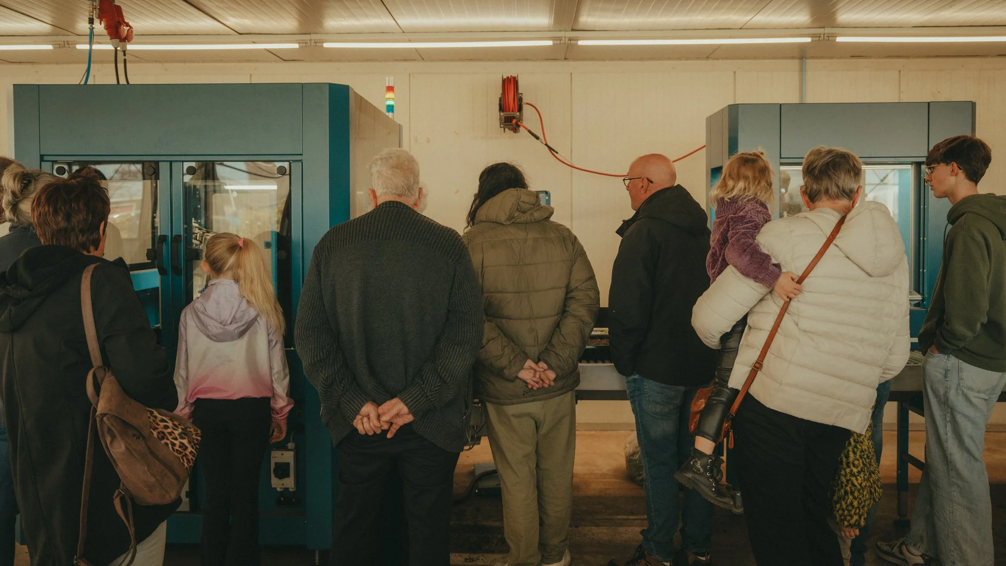 A group of people gathered around a machine or exhibit in a room, possibly at a museum or educational event, observing or learning about it.