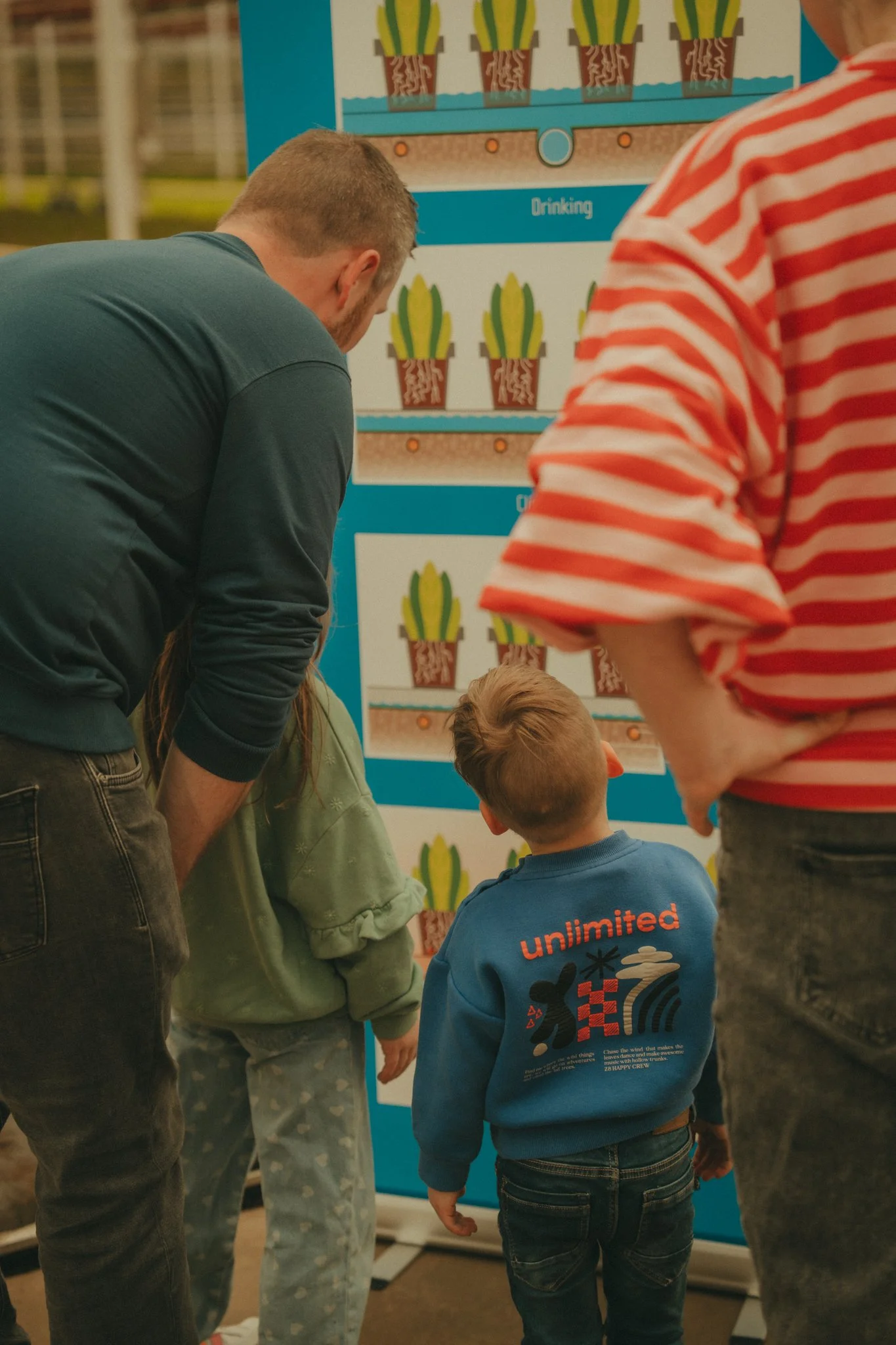 A group of children and adults gathered around a colorful display with pictures of cactus plants and the word 'drinking'.