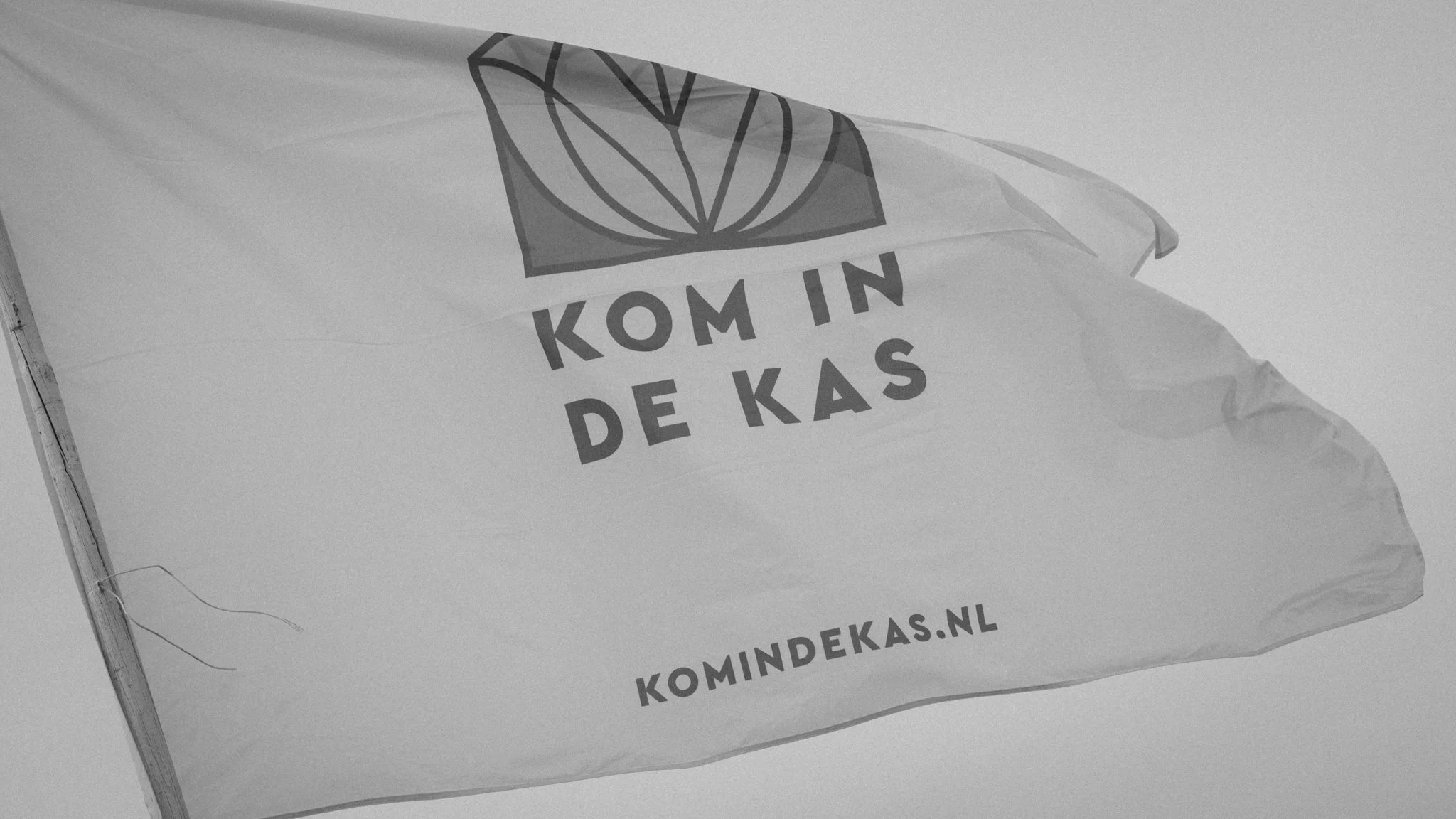 A flag with a logo and text that reads 'KOM IN DE KAS.'