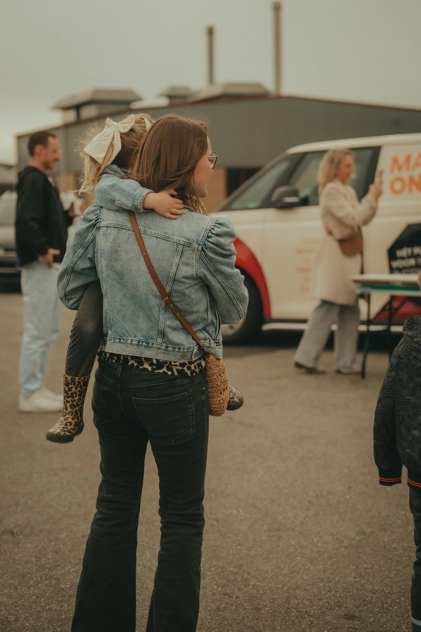 A woman holding a young girl on her back in an indoor setting, with people and a food truck in the background.