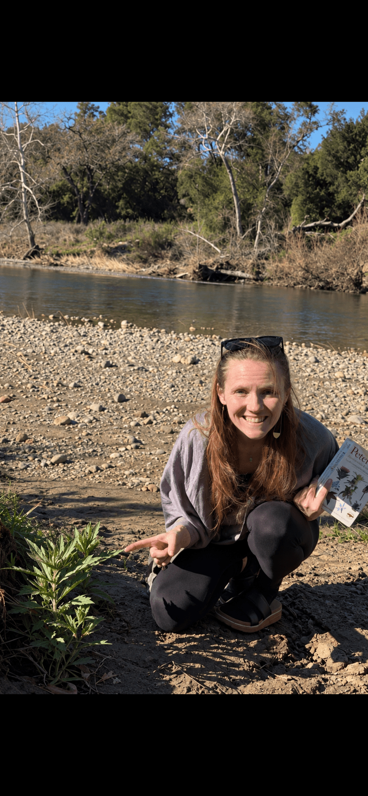 Julia Dyer crouching beside a plant by a river