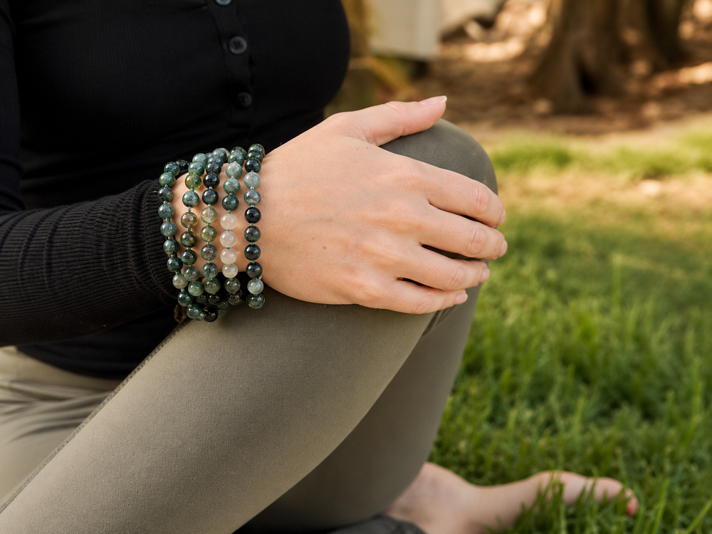 A hand resting on a knee, with layered mala bracelets at the wrist