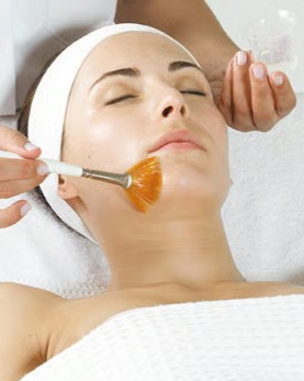 Woman receiving a facial treatment with a brush, lying down with eyes closed and a headband, at a spa or skincare clinic.