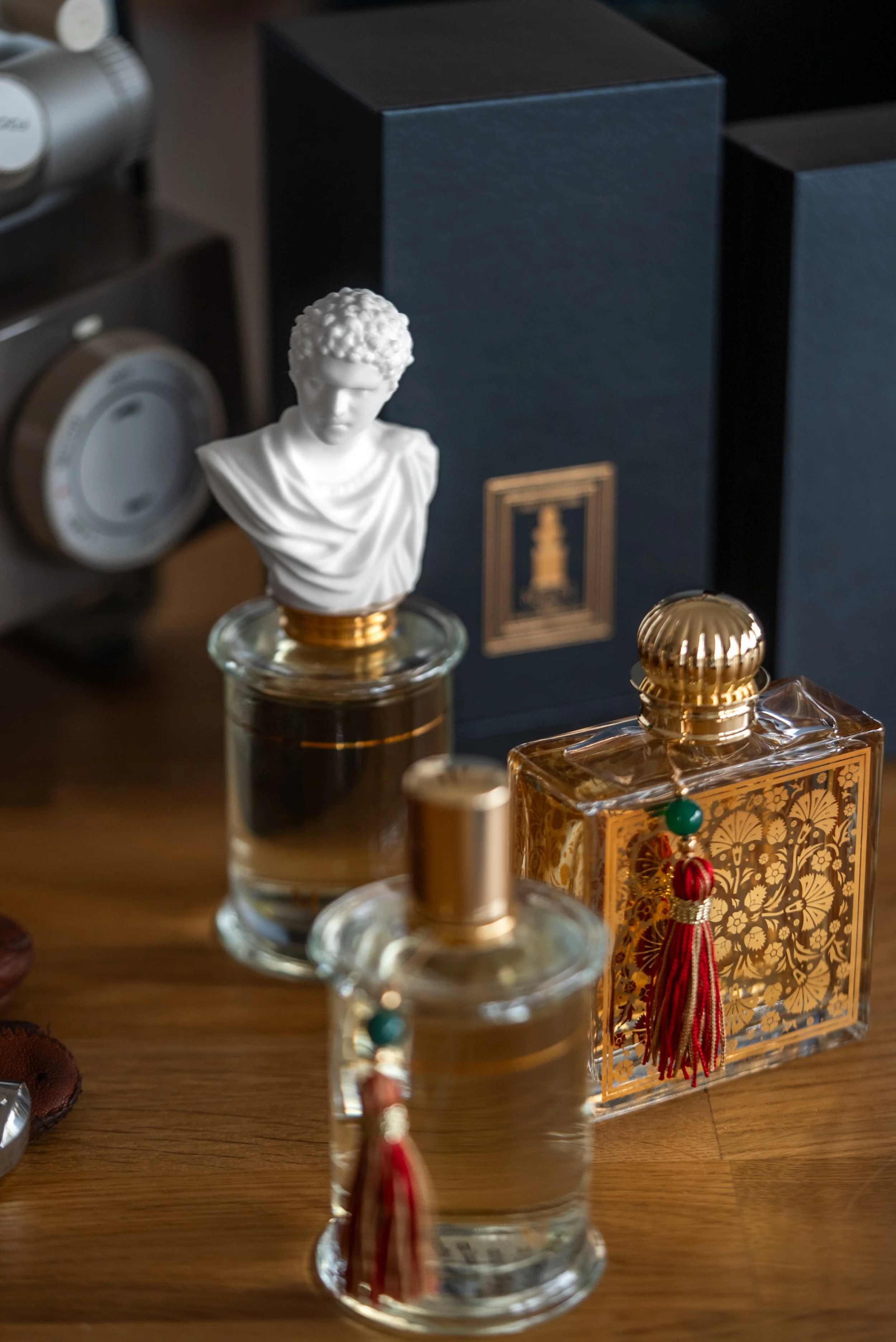 Various perfume bottles on a wooden surface, including a white bust-shaped perfume and dark boxed perfumes in the background.