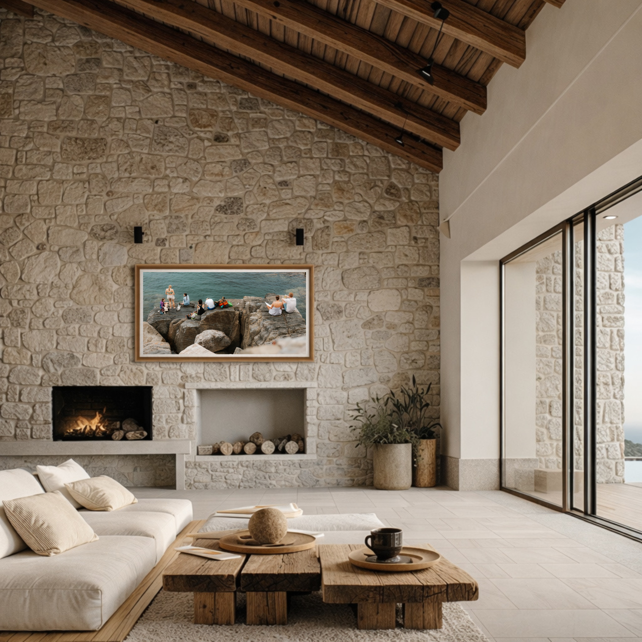 Living room with a stone wall, a wooden ceiling with exposed beams, a white sofa with beige pillows, a wooden coffee table with decorative items, and a fireplace with logs, in front of a large window.
