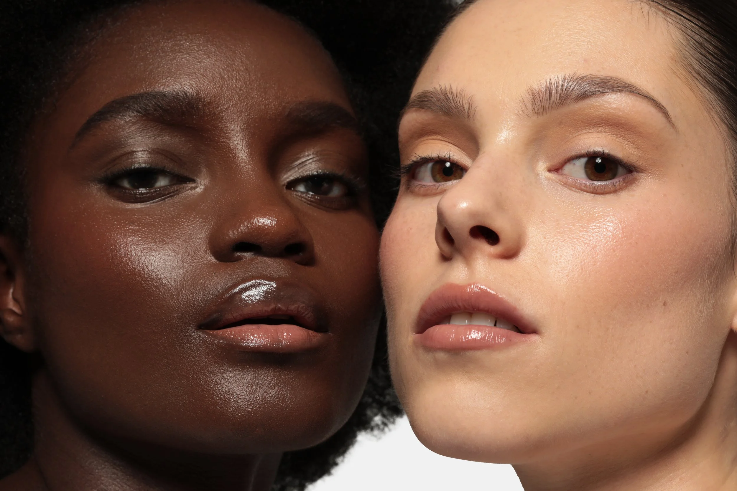 Close-up of two women with contrasting skin tones closely positioned, showing their faces and makeup details.