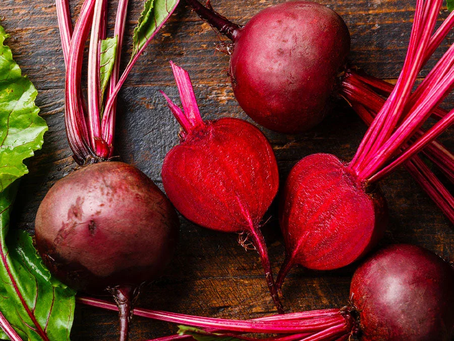 Freshly harvested beets with their green leaves on a rustic wooden surface.