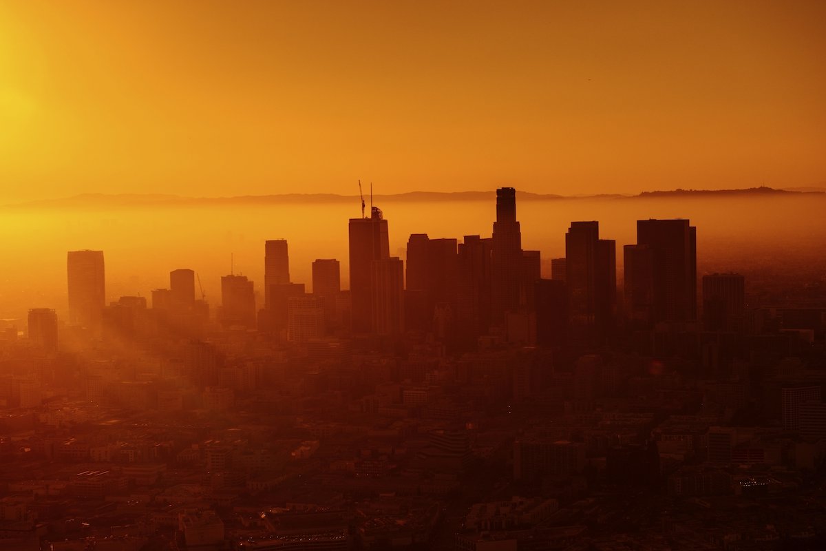 A city skyline during sunset with tall buildings silhouetted against an orange sky.