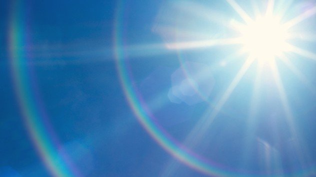 Bright sun shining in a clear blue sky with sunflare and lens artifacts.