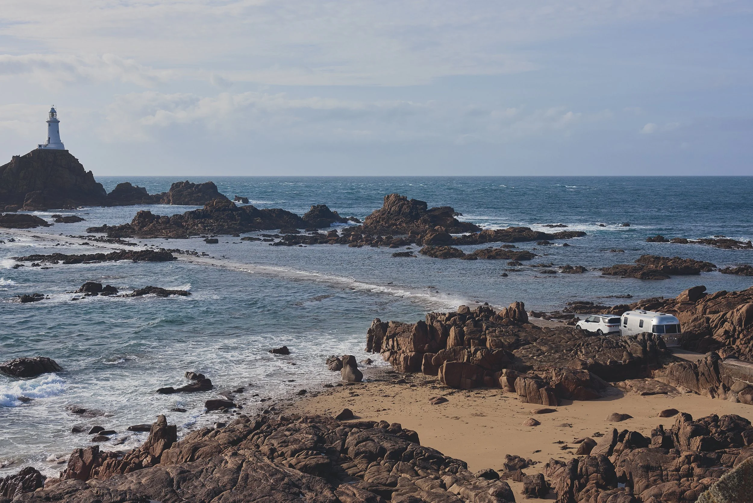 A lighthouse in Jersey with a Land Rover Discovery towing an Airstream caravan