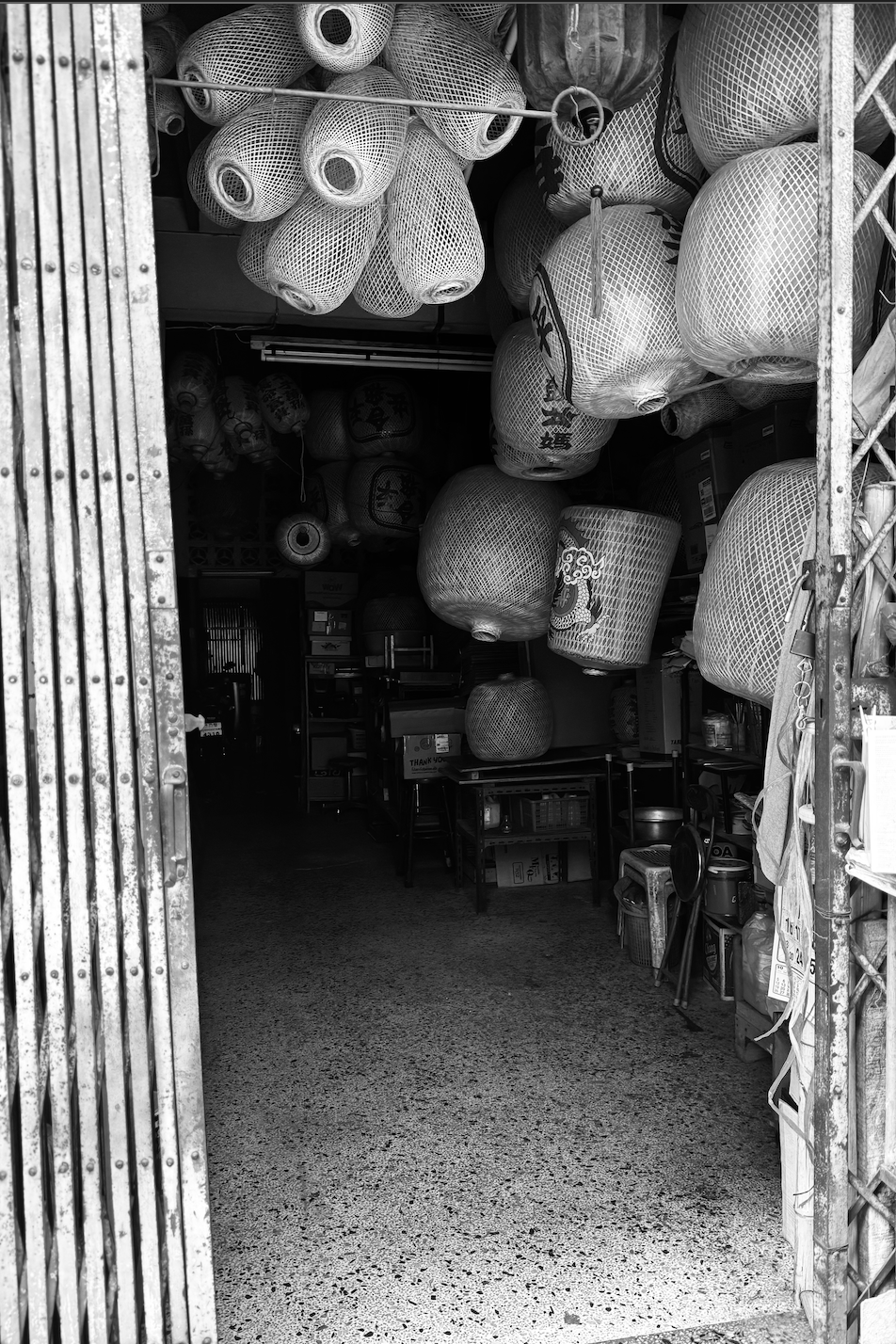 Store entrance with hanging paper lanterns inside, shelves with various items, and a textured floor.