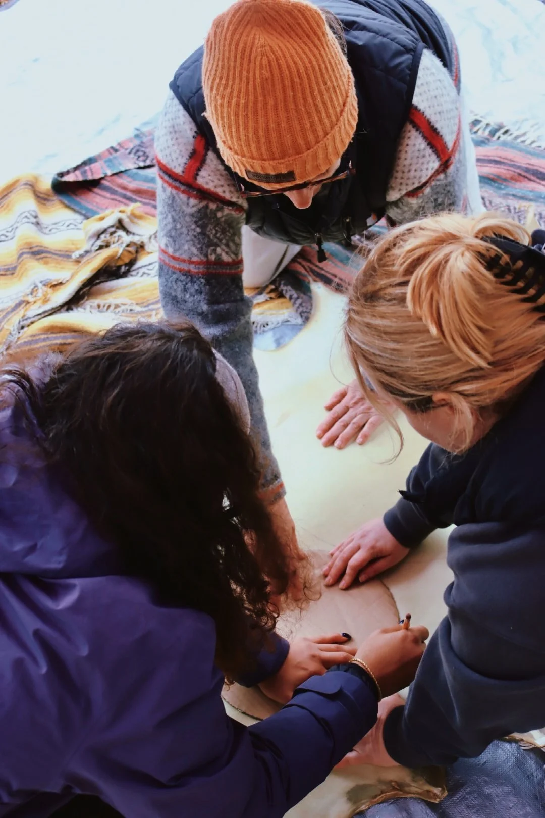 Group of people performing a tattooing session outdoors on a dog, with a blanket laid on snow, during cold weather.