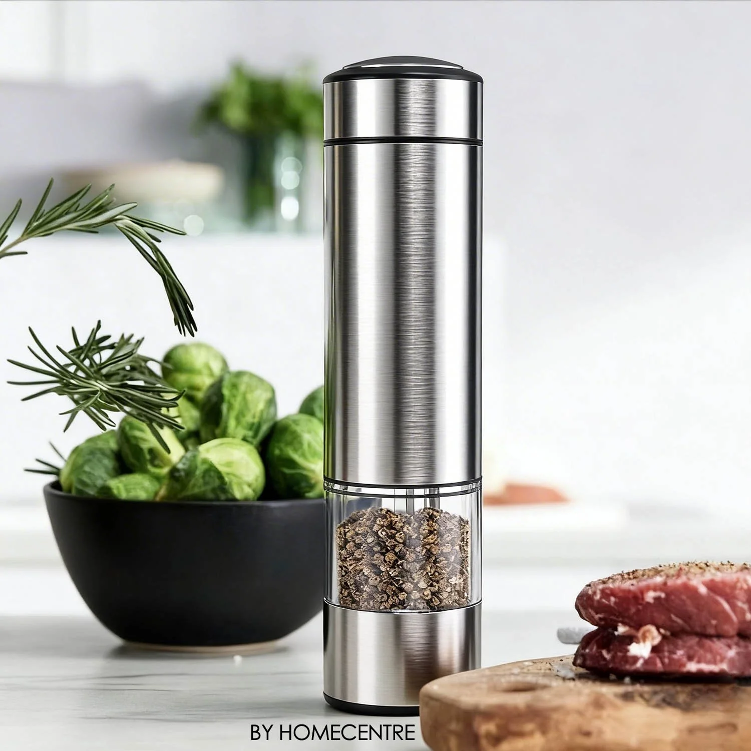 Stainless steel electric pepper grinder with ground pepper, a bowl of Brussels sprouts, rosemary sprigs, and raw meat on a wooden cutting board.
