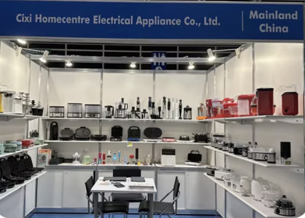 Exhibition booth displaying various kitchen appliances and electronic products, with a sign reading "Cixi Homecentre Electrical Appliance Co., Ltd. Mainland China".