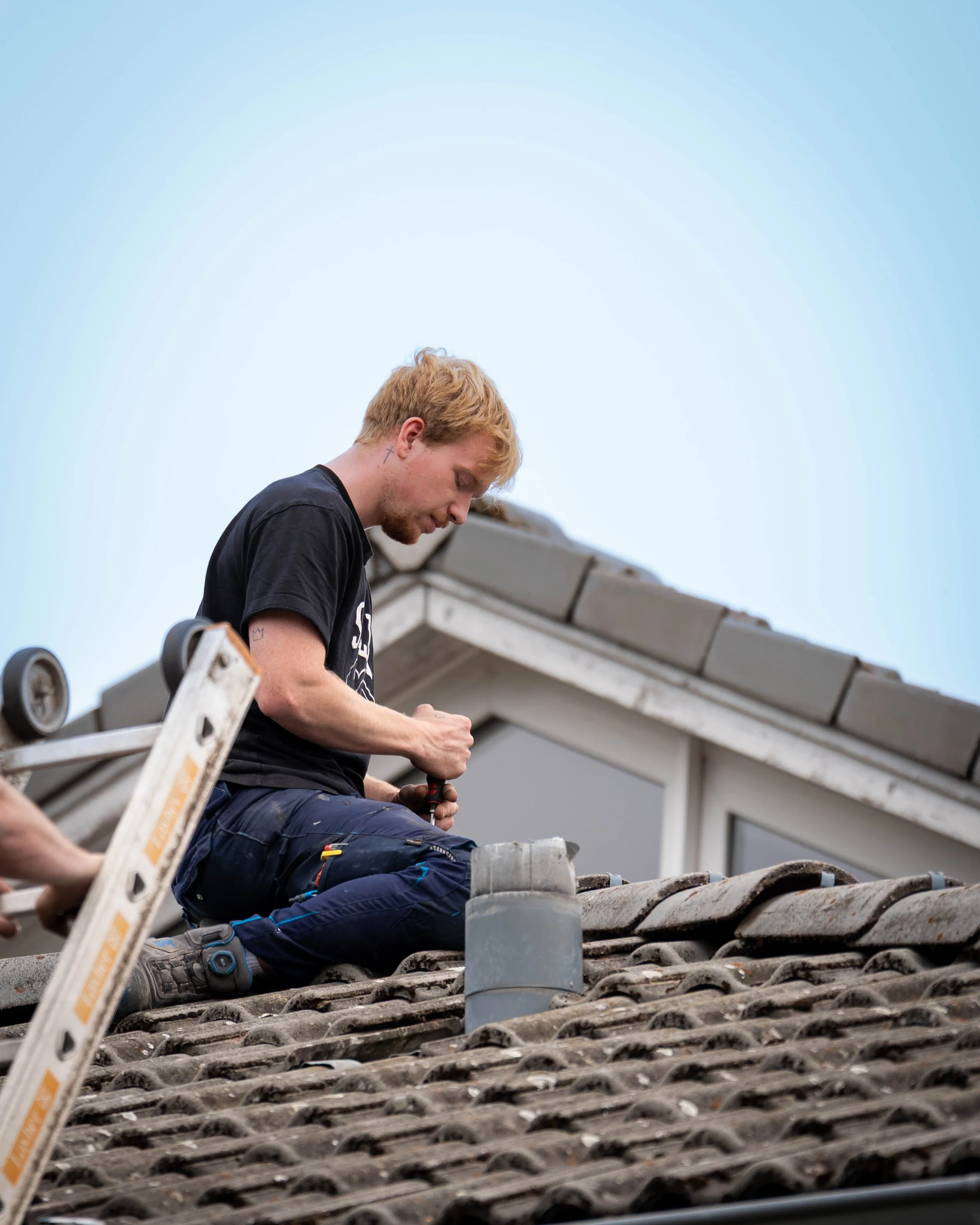 Ein Handwerker sitzt auf einem Dächer und arbeitet an der Reparatur oder Wartung der Dachpfannen.