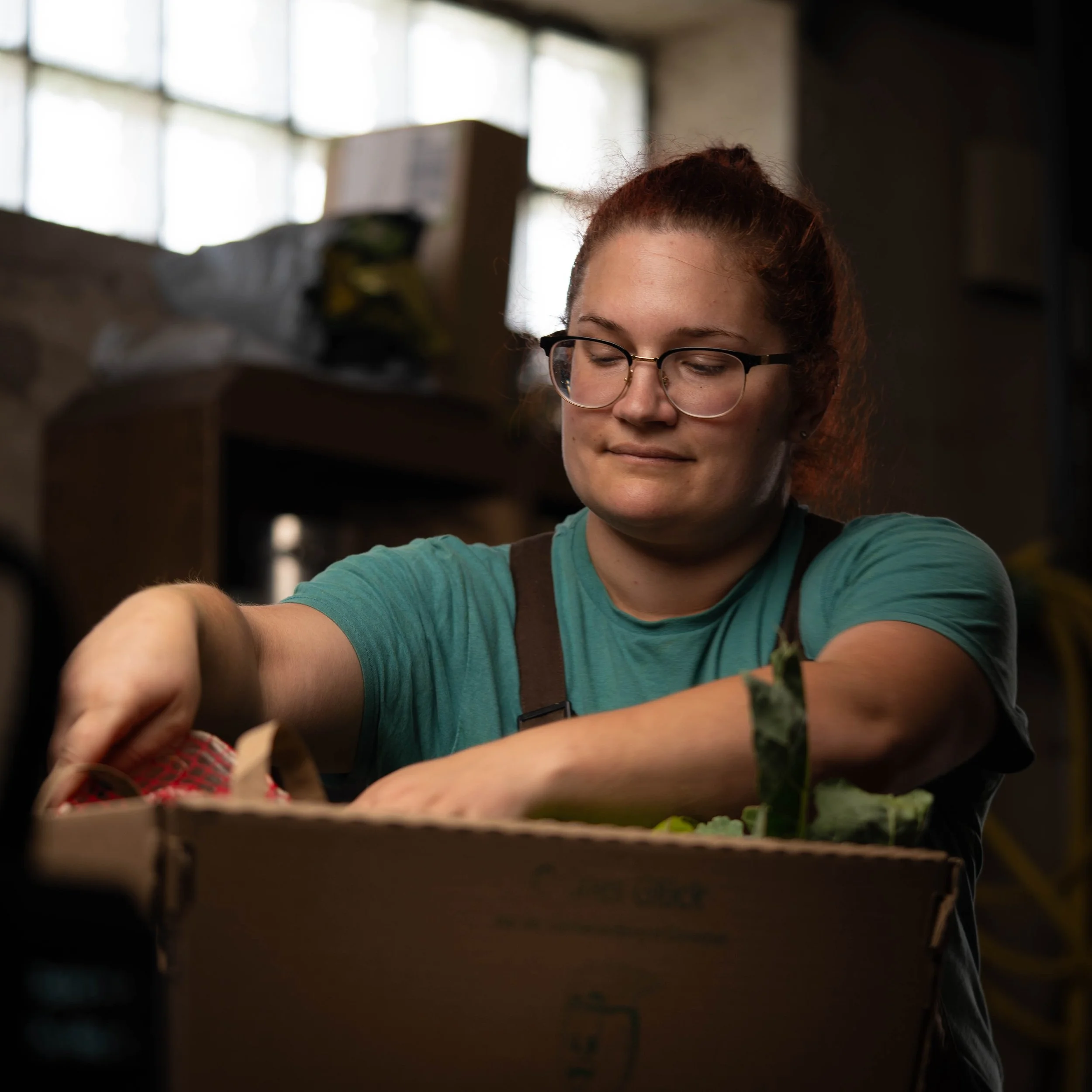 Junge Frau mit Brille beim Verpacken von Gemüse in einer Lagerhalle.