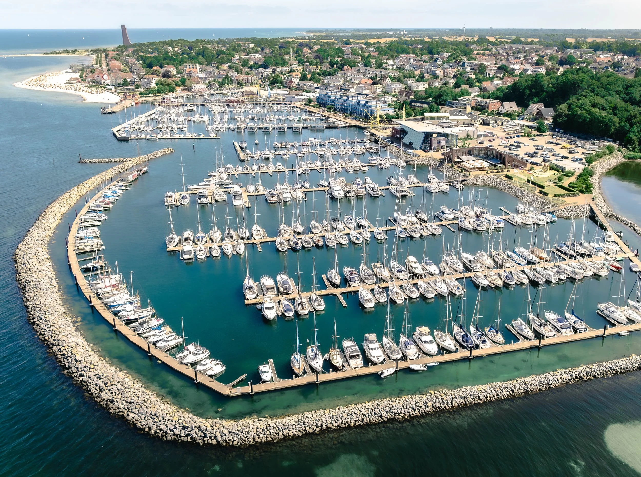 Luftaufnahme eines Yachthafens mit many Booten und Segelbooten, umgeben von Wasser und einer Stadt mit Häusern, Bäumen und Gebäuden im Hintergrund.