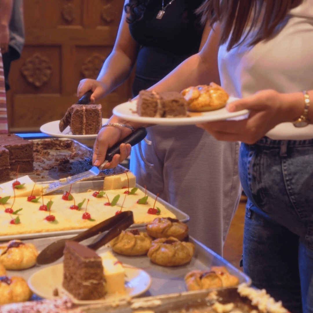 People serving themselves slices of chocolate cake and other desserts at a dessert table.