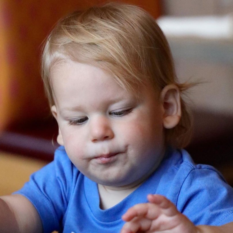 Close-up of a young boy with blond hair wearing a blue shirt, looking down with a thoughtful expression.