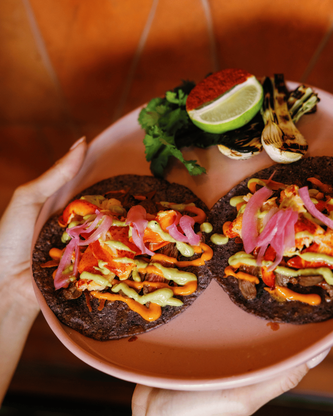Tostadas topped with shredded meat, pink onions, various sauces, and garnished with cilantro, lime, and grilled vegetables.
