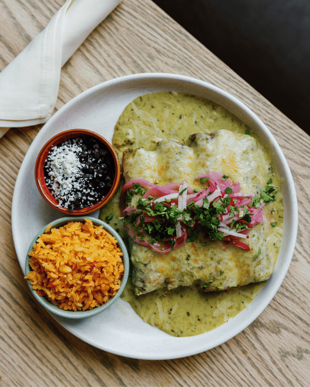 Plate of Mexican food with enchiladas, rice, black beans, and garnishes