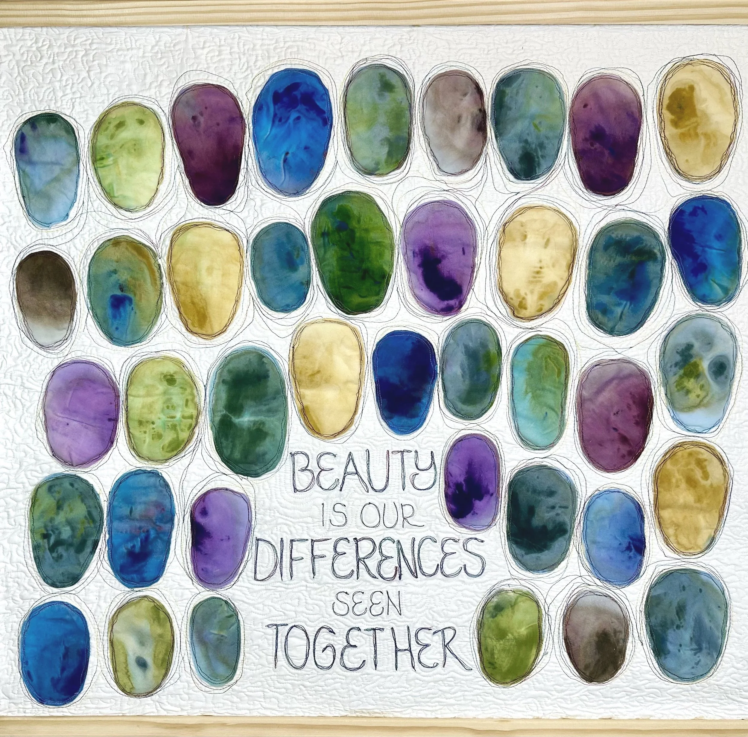 Colorful painted ovals stuffed and appliquéd arranged in rows with handwritten text underneath. The stones are in shades of blue, green, purple, brown, and yellow.