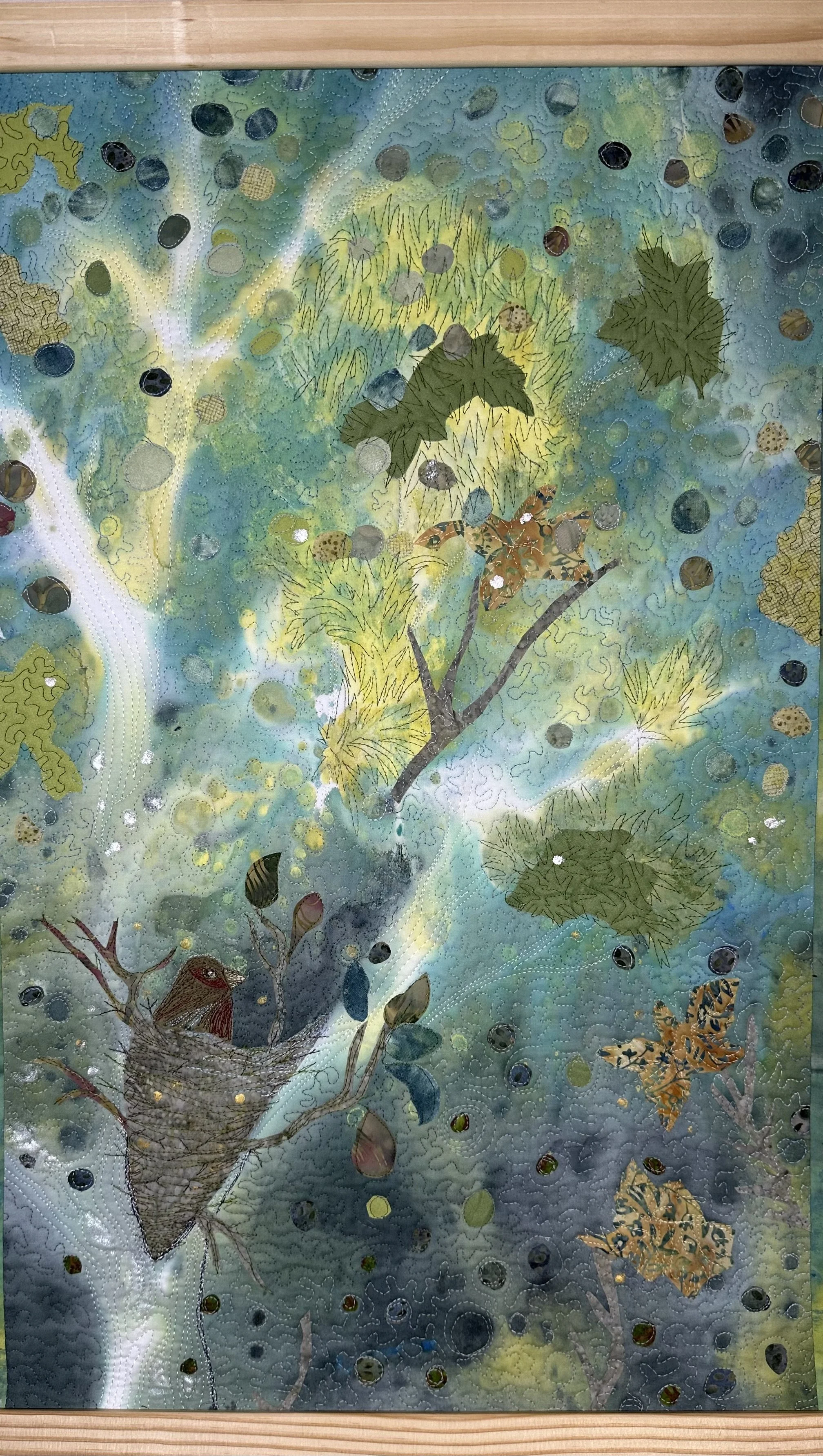 a fiber art collage piece of mystery in the trees where a birds nest is revealed upon closer looking.