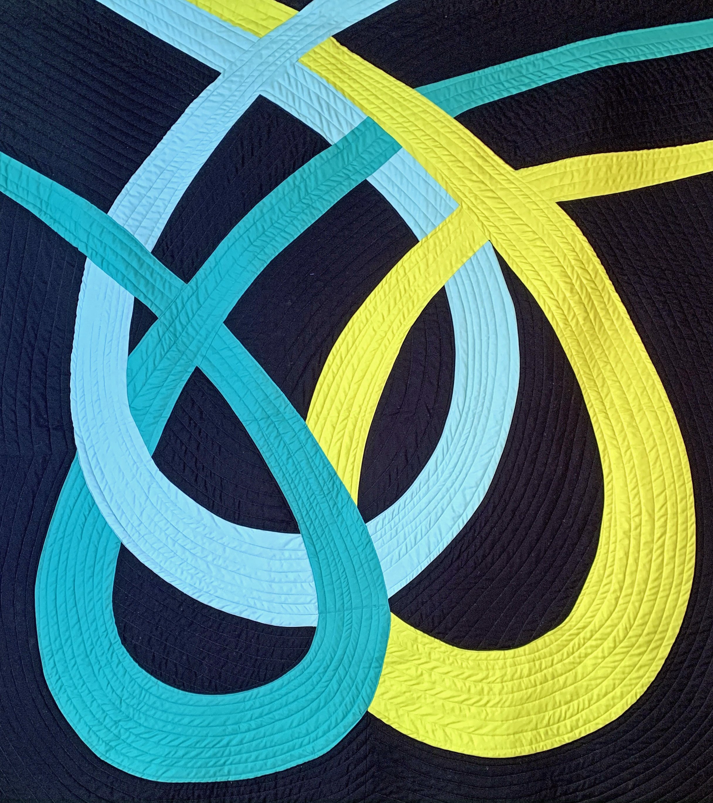 Close-up of a colorful quilt with overlapping curved layers in blue, yellow, and black, featuring quilted stitching.