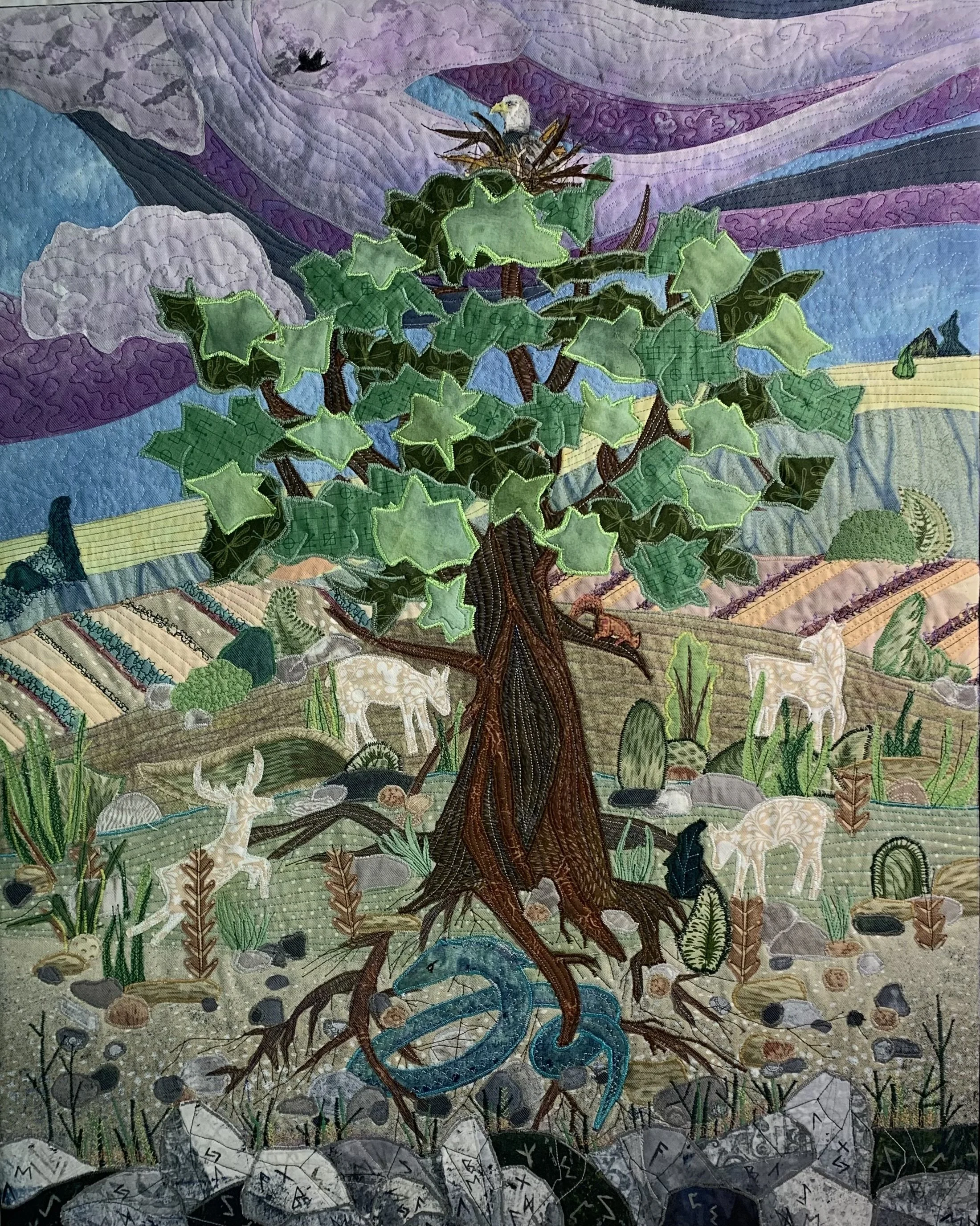 An embroidered fabric art piece depicting a tree with green leaves, a blue stream flowing at the base, and a sky overhead with clouds and a flying bird.