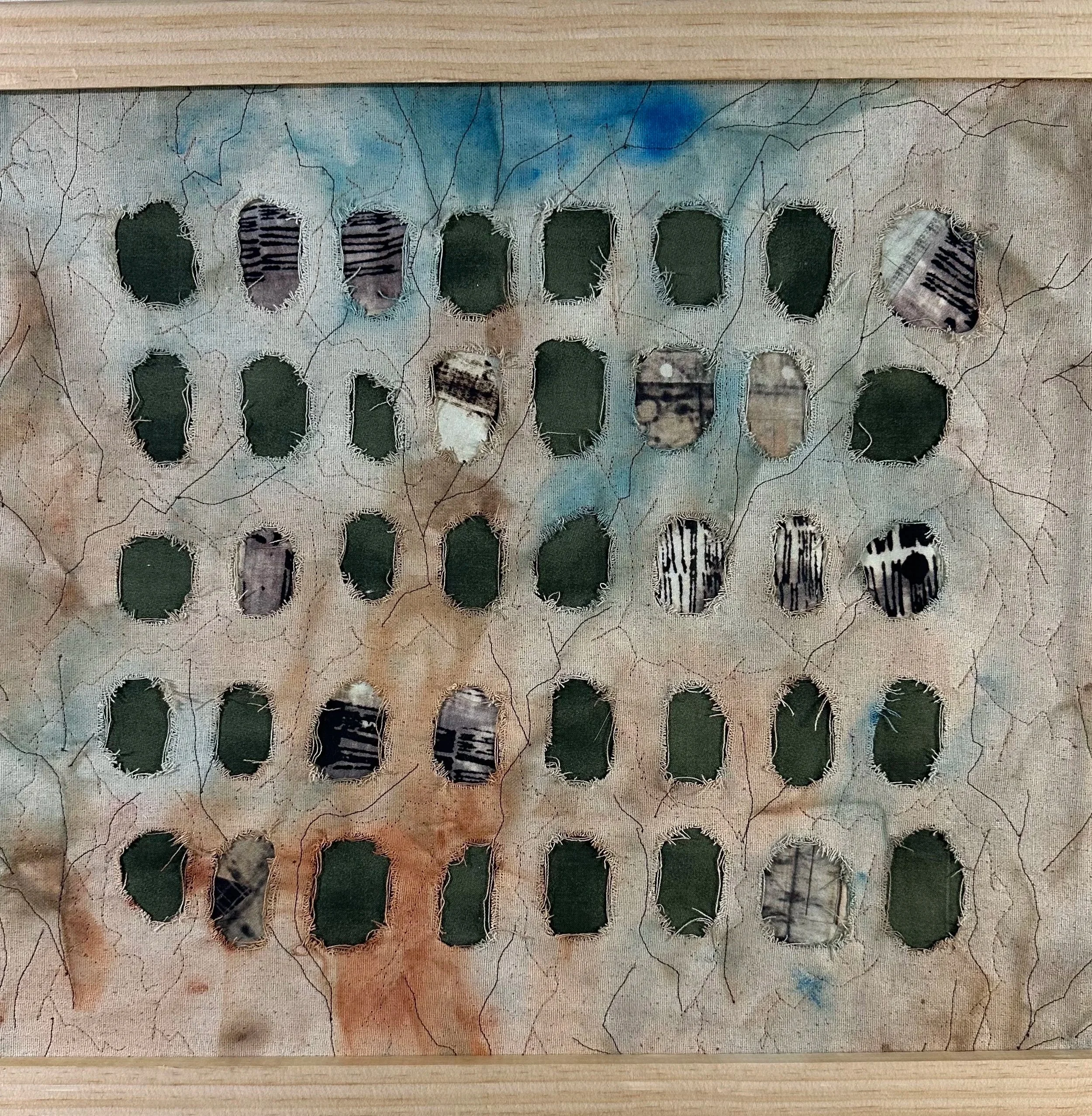 Close-up of a textured fabric with cut-out holes and visible stitching, placed on a wooden surface, with varying colors and patterns visible inside the holes.